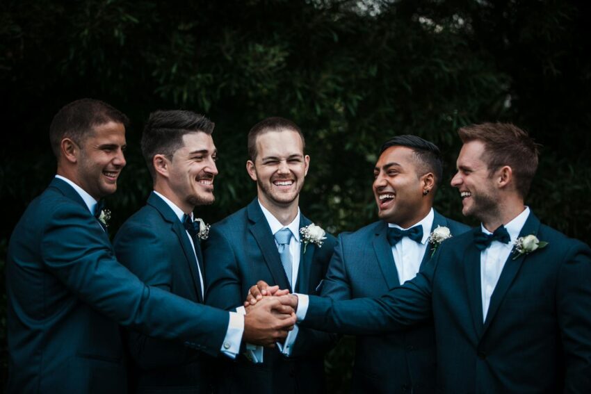 A joyful group of groomsmen celebrate outdoors, dressed in elegant blue suits.